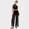 Woman wearing a black halter top and sheer black pants on a white background