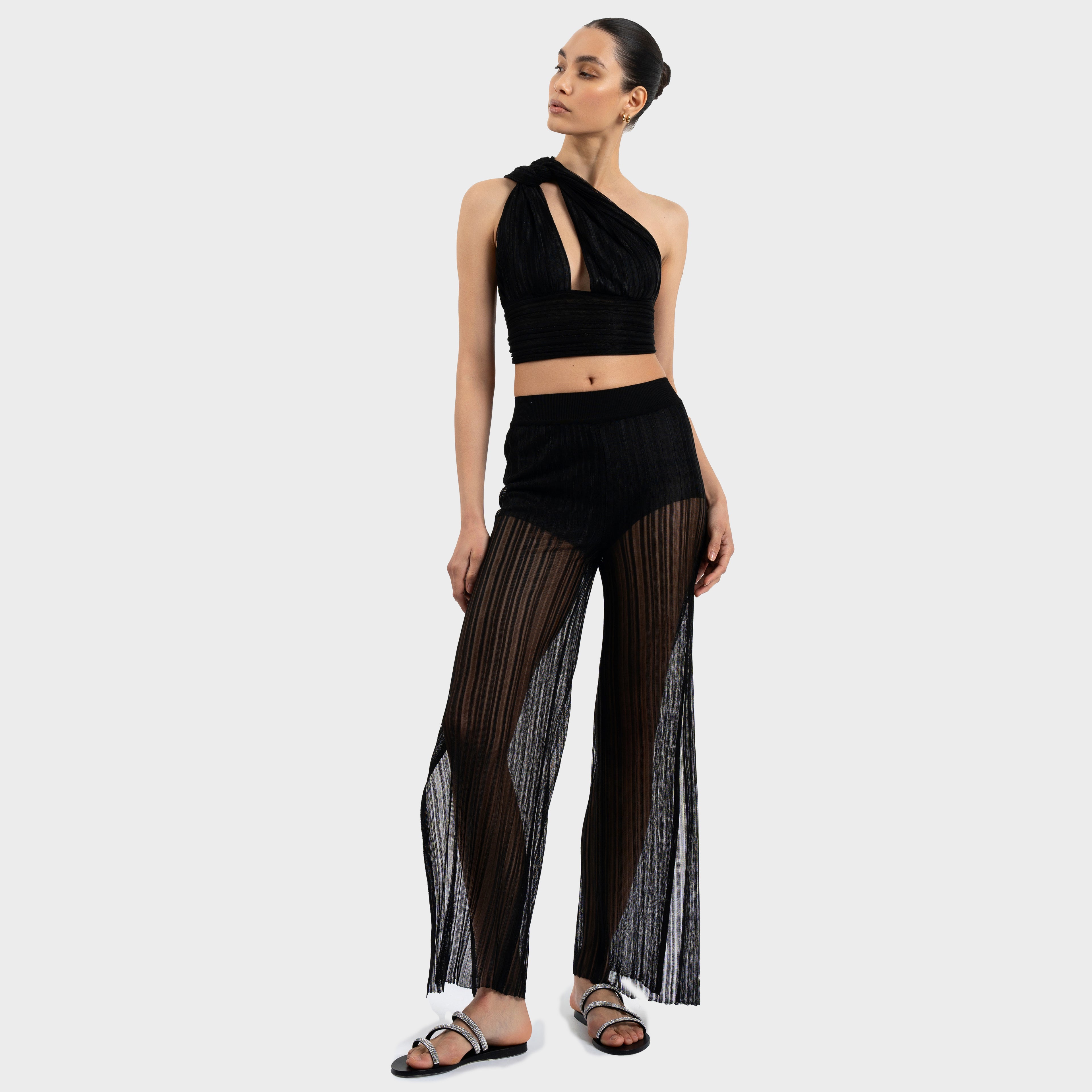 Woman wearing a black halter top and sheer black pants on a white background