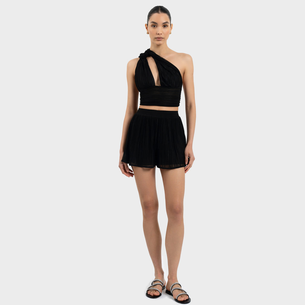 Woman wearing a black one-shoulder top and shorts on a white background
