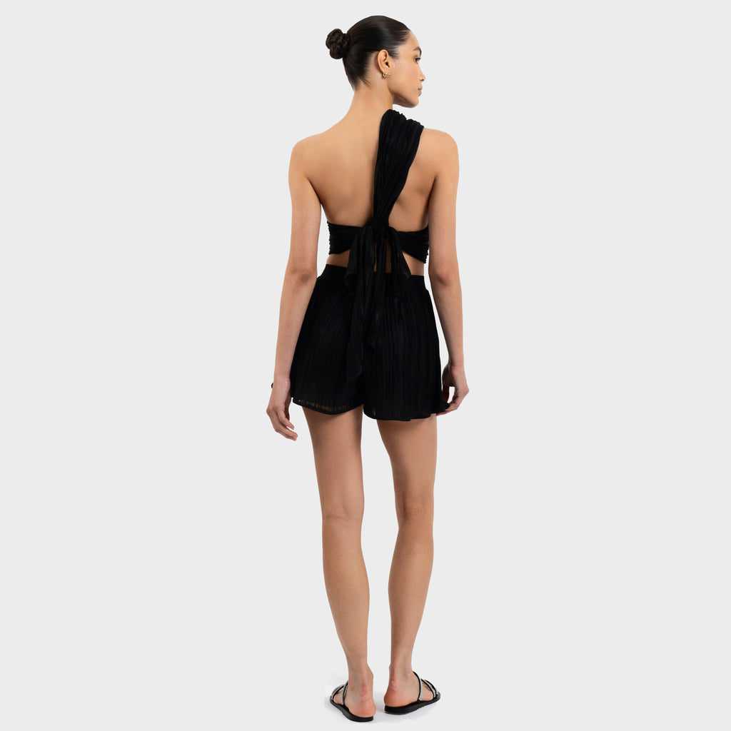 Woman wearing a black open-back top and shorts on a white background