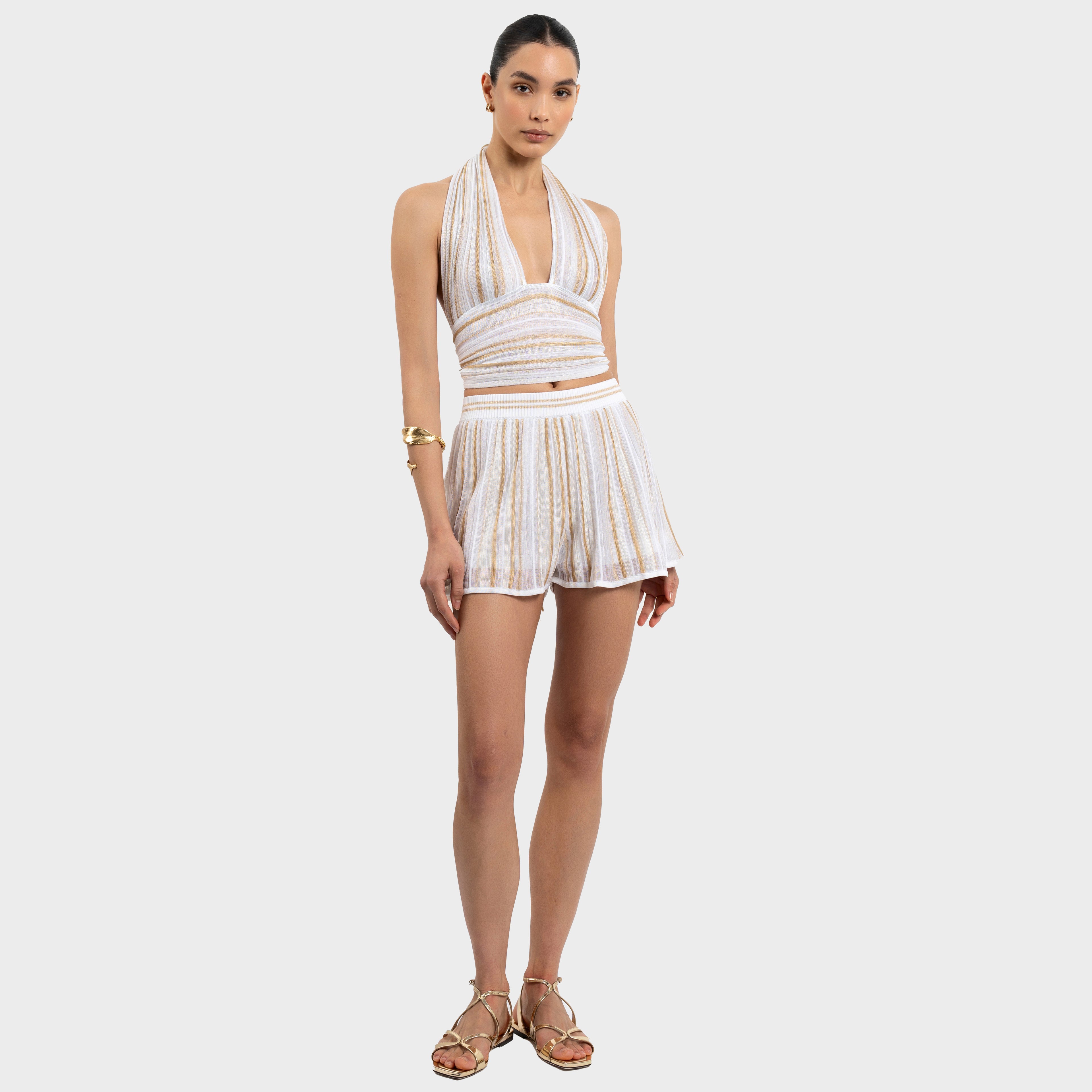 Woman wearing a striped white and gold halter neck top and shorts outfit on a white background